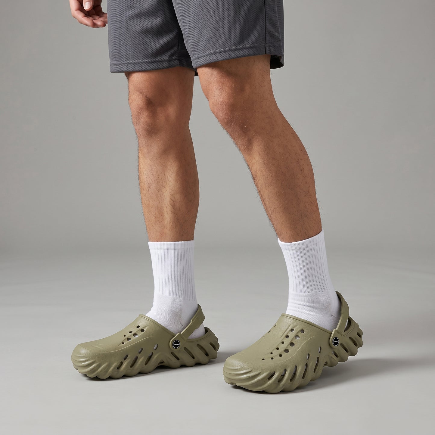 Person wearing Sage Green Crocs & clogs with white socks on a neutral background