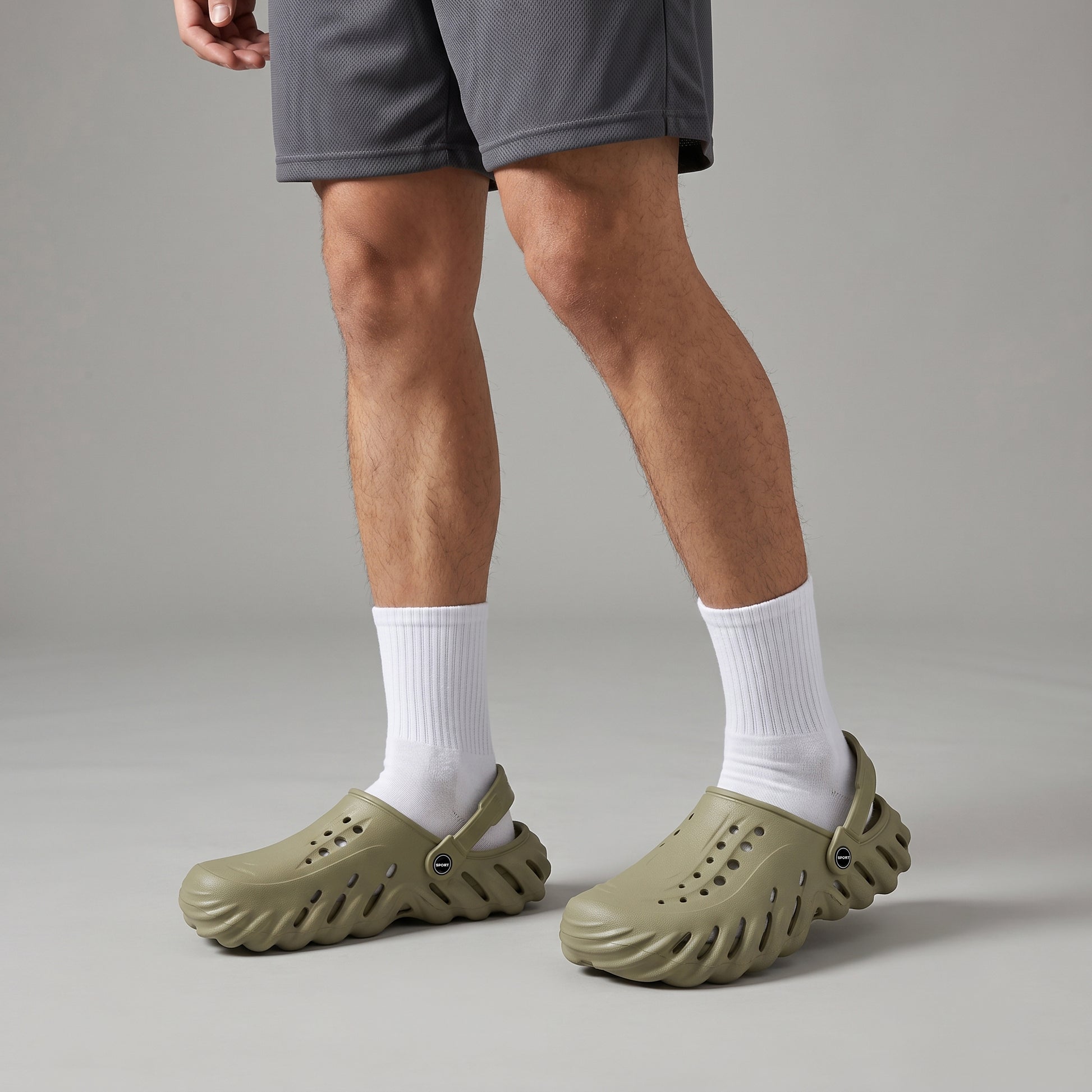 Person wearing Sage Green Crocs & clogs with white socks on a neutral background