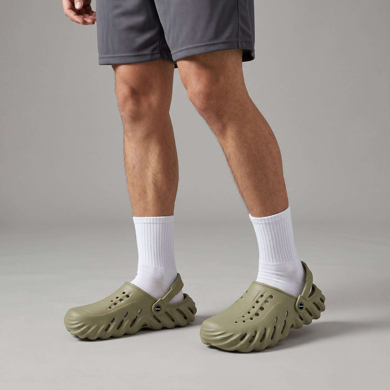 Person wearing Sage Green Crocs & clogs with white socks on a neutral background